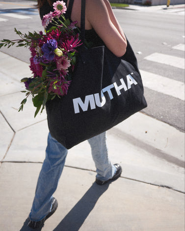Image of a woman walking across the street with the MUTHA Tote Bag filled with flowers on her shoulder