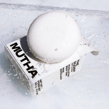 Stylish image of the Nudist Exfoliating Body Bar on top of its box with splashing water