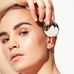 Image of a model holding a Metal Applicator with Cream on it near the face