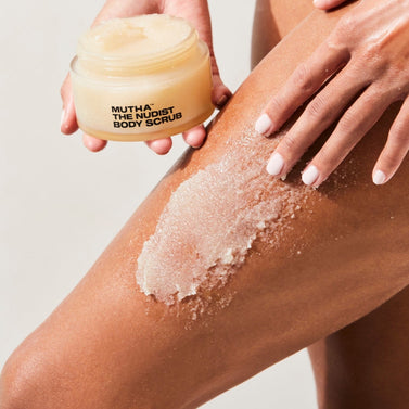Image of a model applying a swipe of the NUDIST Body Scrub to the thigh while holding the jar in the other hand