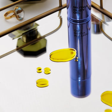 Stylish image of the Body Oil on a mirrored counter surface with droplets of the Body Oil on the mirror