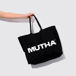 Image of a hand holding the MUTHA Tote Bag by the strap