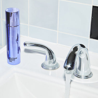 Stylish image of the Body Oil on a sink counter with water running from the faucet