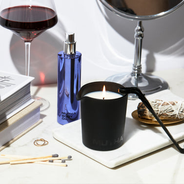 Stylish image of the MUTHA™ Aphrodisiac Massage Candle, Body Oil, red wine, and miscellaneous dresser items