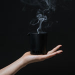 Stylish image of a hand holding the MUTHA™ Aphrodisiac Massage Candle with smoke