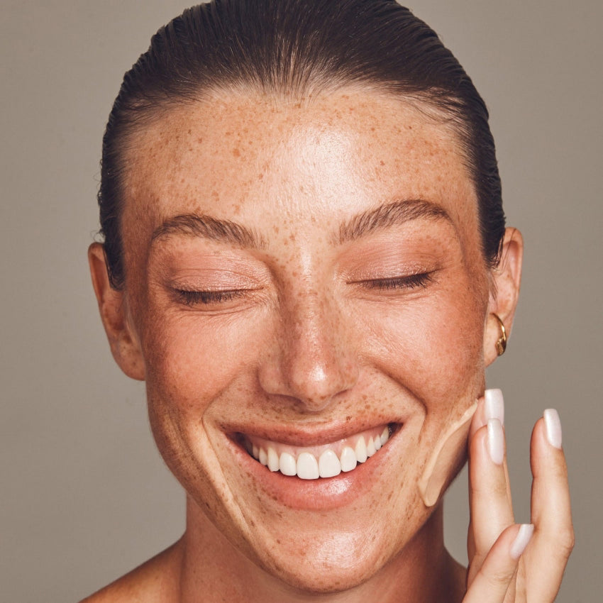 Woman applying cream to her face with a neutral background